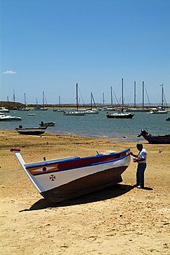 PORTUGAL, ALGARVE, ALVOR, Fisherman painting his boat