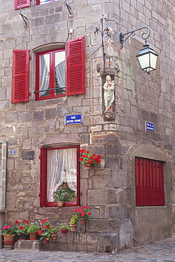 Statue of the Madonna and Child on a house with red shutters on a street corner in Besse en Chandesse, in the Auvergne, France, Europe