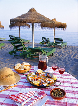 Paella with olives, bread and sangria on a table on the beach in Andalucia, Spain 
