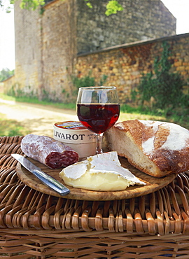 Still life of bread, glass of red wine, cheese and sausage, picnic meal on top of a wicker basket, in the Dordogne, France, Europe