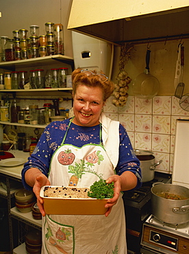 Portrait of a woman in an apron, holding a dish, smiling and looking at the camera, in the kitchen of a restaurant in Provence, France, Europe