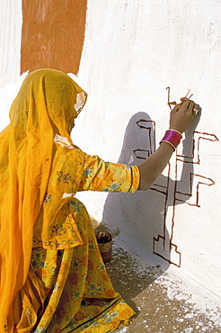 Woman painting design on a wall in a village near Jaisalmer, Rajasthan state, India, Asia