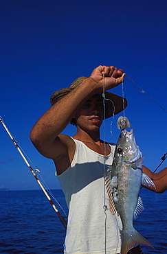 Young man with fish caught on a line, northeast coast, island of Praslin, Seychelles, Indian Ocean, Africa