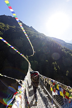 Porter crossing a suspension bridge decorated in Tibetan prayer flags, Sagarmatha National Park, UNESCO World Heritage Site, Khumbu Valley, Nepal, Asia