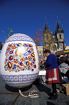 A Moravian woman decorating a large egg with Easter designs on the Old Town Square, with Tyn Church in the background, Prague, Czech Republic, Europe