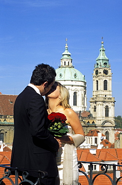 Portrait of a couple kissing after getting married at Vrtbovska Garden with Baroque St. Nicholas church in background, Mala Strana, Prague, Czech Republic, Europe