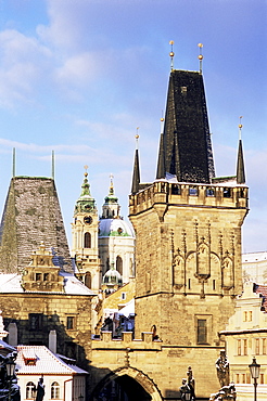 Snow-covered Romanesque and Gothic Malostranske Bridge towers and in the background the towers of the Baroque St. Nicholas church, Mala Strana, Prague, Czech Republic, Europe