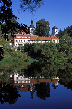 View across water to castle and village of Karlstejn reflected in Berounka River, Central Bohemia, Czech Republic, Europe