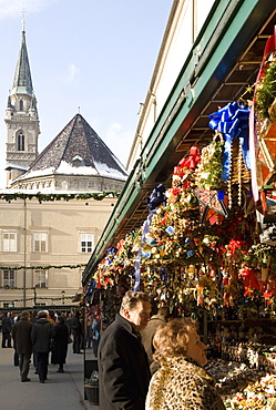 Stall selling Christmas decorations with towers of Franziskanerkirche churchbehind, Historical Salzburg Christkindlmarkt (Christmas market), Domplatz, Salzburg, Austria, Europe