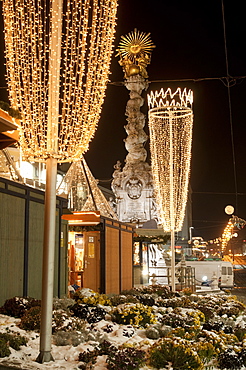 Snow-covered flowers, Christmas decorations and Baroque Trinity Column (Dreifaltigkeitssaule) at Christmas Market, Hauptplatz Square, Linz, Oberosterreich (Upper Austria), Austria, Europe