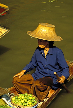 Portrait of a Thai woman vendor in straw hat with a basket of limes, on boat in canal at the Damnoen Saduak floating market, Ratchaburi, Thailand, Southeast Asia, Asia