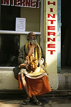 Sadhu (Hindu holy man) sitting outside an internet cafe, Varanasi (Benares), Uttar Pradesh state, India, Asia