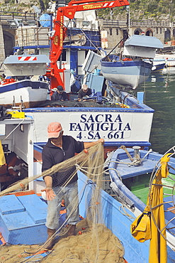 A fisherman gathers the nets after being at sea in the port of Cetara, Amalfi Coast, Campania, Italy. Behind him, a boat with a very typical name: Holy Family.