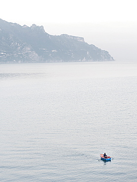 A lonely fisherman paddles on his small boat off the coast of Atrani, Amalfi Coast, Campania, Italy, Europe