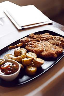 Cotoletta Milanese cooked by Restaurant Brunello in Milano served with baked french potatoes and tomatoes salad and a glass of mild red wine.