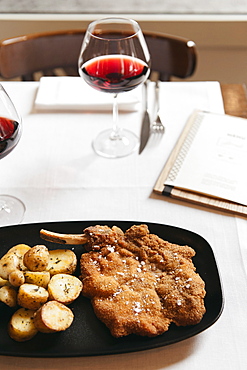 Cotoletta Milanese cooked by Restaurant Brunello in Milano served with baked french potatoes and tomatoes salad and a glass of mild red wine.