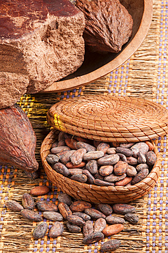 Raw chocolate, cocoa beans and cocoa pods in a woven vegetable fiber box.