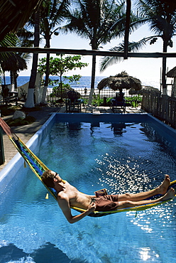 Tourist in hammock relaxing over pool, Monterico, Guatemala, Central America