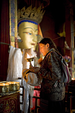 Woman adding yak butter from her butter lamp to those in the Buddhist temple, Meru Nyingba monastery, Bharkor, Lhasa, Tibet, China, Asia