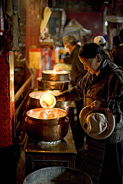 Woman adding the melting yak butter from her lamp to those of the temple, Meru Nyingba monastery, Bharkor, Lhasa, Tibet, China, Asia