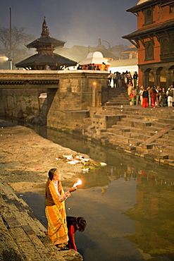 Two women making offerings (puja) before dawn by the Bagmati river, outside the Shiva temple during the Hindu festival of Shivaratri, Pashupatinath, Kathmandu, Nepal, Asia