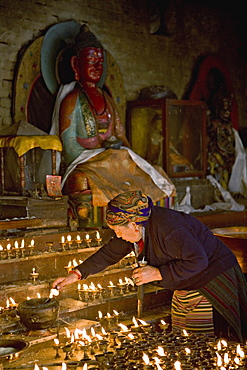 Old woman lighting butter lamps in a small temple on the north side of Boudha or Bodhnath stupa, Tibetan New Year (Lhosar), Kathmandu, Nepal, Asia