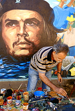 An artist painting a wall mural featuring a portrait of the revolutionary hero Che Guevara on a street in Baracoa, Cuba