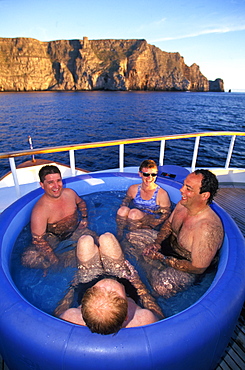 Scuba divers relaxing in a hot tub with the volcanic cliffs of Wolf Island beyond one of the newest and most northerly of the Islands, Galapagos Islands, Ecuador