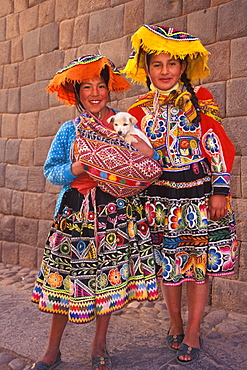 Two young Indian girls in traditional dress in front of a finely cut Inca Wall on Calle Loretto in the heart of the colonial center, Cuzco, Highlands, Peru