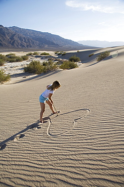 Woman drawing a heart in the sand, Sand Dunes Point, Death Valley National Park, California, United States of America, North America