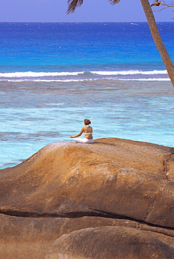 Young woman meditating on rock, Seychelles, Indian Ocean, Africa