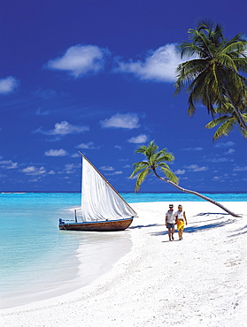 Couple walking on tropical beach and traditional dhoni, Maldives, Indian Ocean, Asia