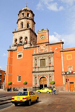 Mexico, Bajio, Queretaro, The church of San Francisco brightly coloured exterior facade with taxis and cyclist on road in foreground.