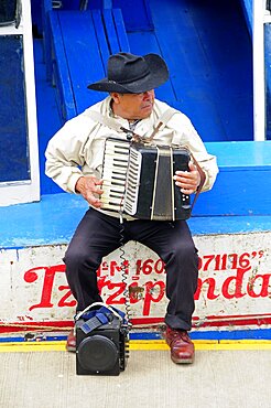 Mexico, Michoacan, Patzcuaro, Lago Patzcuaro Musician playing the accordion sitting on painted boat.