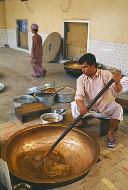 OMAN  Food  Man stirring in butter to Halva mixture