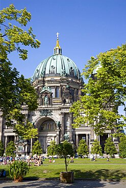 Germany, Berlin, Mitte, Museum Island. Berliner Dom, Berlin Cathedral, with green copper domes and people on the grass in Lustgarten.