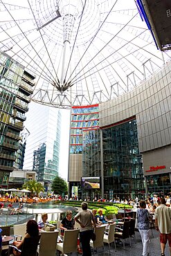 Germany, Berlin, Mitte, Potsdamer Platz, The Sony Centre designed by architect Helmut Jahn with the canopy over the central Forum of restaurants, offices, cinemas, shops and apartments with people eating at tables.