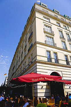 Germany, Berlin, Mitte, the rebuilt five star Hotel Adlon Kempinski on the corner of Unter den Linden and Pariser Platz with people at tables under umbrellas.