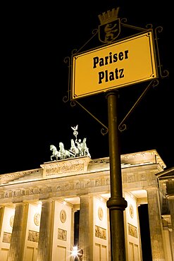 Germany, Berlin, Mitte, Brandenburg Gate or Brandenburger Tor and roadsign for Pariser Platz illuminated at night leading to Unter den Linden and the Royal Palaces with the Quadriga of Victory on top. The only remaining of the original 18 gates in the Berlin Customs Wall.