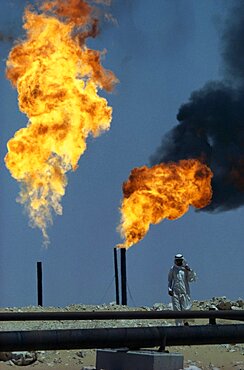 SAUDI ARABIA  Industry Flaming gas on oil field with man standing behind pipe in foreground.