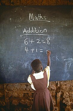 GHANA West Education Child in primary school maths class writing sums on blackboard with chalk.  addition