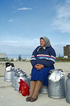 ESTONIA Work Woman sitting on milk cans waiting for ferry on the Baltic Coast.