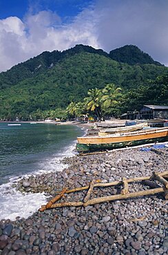 DOMINICA Windward Islands Soufriere Bay Scotts Head fishing village. View across stoney beach lined with wooden fishing boats and huts towards palmtrees and tree covered hillside