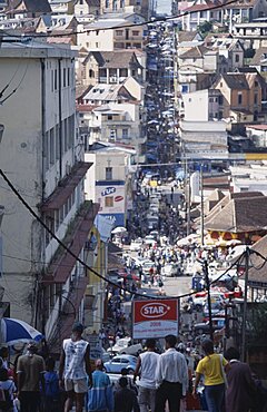 MADAGASCAR Antananarivo Downtown area. People walking down towards a busy road running between buildings and shopfronts filled with people and cars