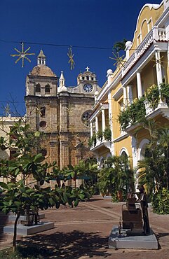 COLOMBIA Bolivar Cartagena Plaza de San Pedro Claver.  Yellow and white colonial facade of building on right with part view of Church of San Pedro Claver beyond.  Sculpture and trees in foreground.  Saint Peter Claver American Colombian Columbia Hispanic Latin America Latino Religion Religious South America