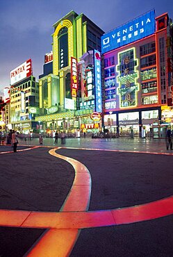 CHINA  Shanghai Nanjing Lu.  Busy street scene at night with illuminated neon signs and advertising and ribbon of pink / orange lit pavement across square in the foreground.