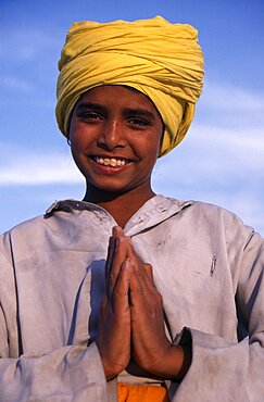 Portrait of smiling Sikh boy wearing yellow turban making gesture of greeting or namaste with his hands, Amritsar, Punjab, India