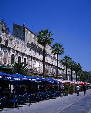 The restored walls of the Diocletian Palace with umbrella coverred cafe tables on the pavement, Split, Croatia