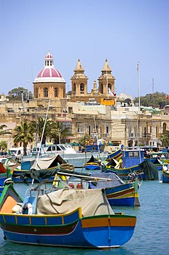 Fishing village harbour on the south coast with colourful Kajjiki fishing boats and the Church dedicated to Our Lady of the Rosary The Madonna of Pompeii, Marsaxlokk, Malta