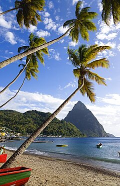 Fishing boats on the beach lined with coconut palm trees with the town and the volcanic plug mountain of Petit Piton beyond, Soufriere, St Lucia